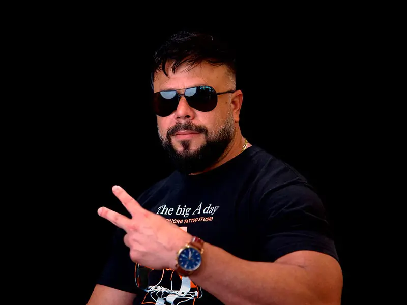 Portrait of Jarlen Perez from Alex Chiong Tattoo Studio in North Miami, Florida, wearing sunglasses and making a peace sign