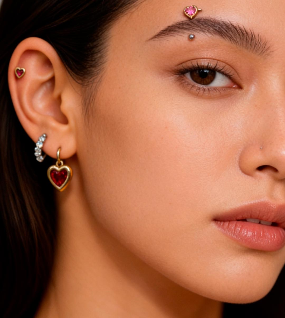 Close-up of a woman with multiple ear, eyebrow, and nose piercings featuring heart-shaped jewelry at Alex Chiong Tattoo Studio in North Miami.